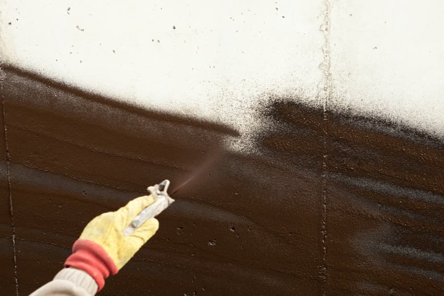 Worker spraying waterproofing sealant onto basement wall