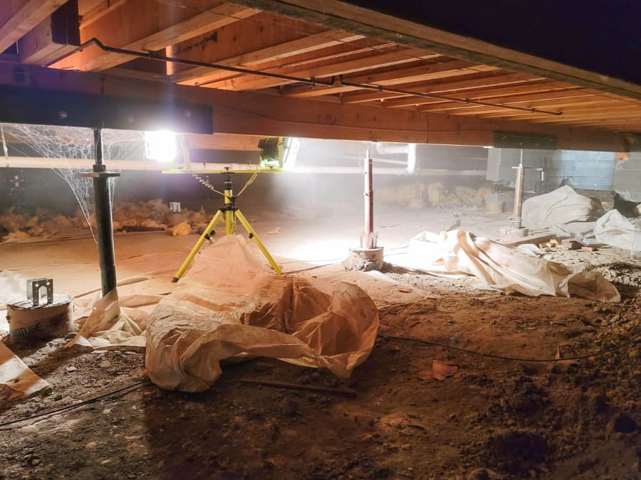 Industrial lights shining in crawl space with plastic barriers being installed